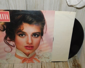 May include: A vinyl record album cover featuring a woman with long brown hair and a pink and white lace collar. The album title "Sylvia" is printed in red on the top left corner of the cover.