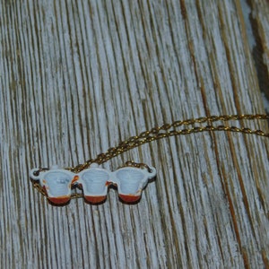 May include: A gold chain necklace with a pendant featuring three miniature teacups with white interiors and red and orange accents.
