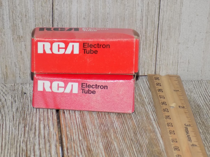 May include: Two red RCA Electron Tube boxes stacked on top of each other. The boxes have white text and logos. A wooden ruler is next to the boxes, showing inch measurements.