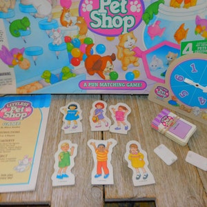 May include: A "Littlest Pet Shop" board game set. The box features cartoon pets and the text "A Fun Matching Game!". Includes game pieces, cards, and a spinner. The game is for ages 4 and up, for 2 to 4 players.