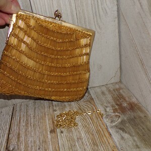 May include: A gold beaded evening bag with a chain strap. The bag is made of small, round beads that are sewn together in a pattern. The chain strap is attached to the bag with a clasp.