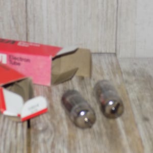 May include: Two vintage RCA Electron Tube vacuum tubes with a red and white box. The box is open, revealing the tubes and the text "Electron Tube". The tubes are glass with a dark interior.