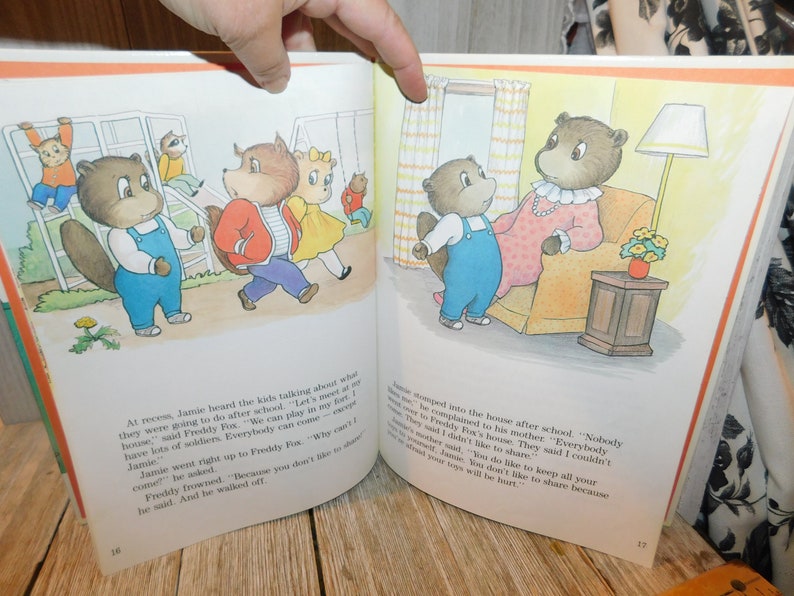 May include: An illustrated children's book page featuring a group of brown bears playing on a jungle gym and a family of bears in their home. The text on the page reads, "At recess, Jamie heard the kids talking about what they were going to do after school. "Let's meet at my house," said Freddy Fox. "We can play in my fort. I have lots of soldiers. Everybody can come."  "Why can't I come?" Jamie asked. Freddy frowned. "Because you don't like to share." he said. And he walked off."