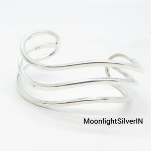 May include: A polished silver cuff bracelet featuring three distinct, wavy, parallel bands that curve to form an open-ended structure. The metal has a smooth, reflective finish. The text MoonlightSilverIN is visible in the bottom right corner.