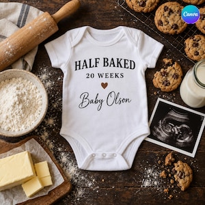 May include: A white short-sleeved baby bodysuit featuring the black text "HALF BAKED 20 WEEKS" with a small brown heart and the name "Baby Olson" in a script font, centered on the front of the garment with three snaps at the bottom.