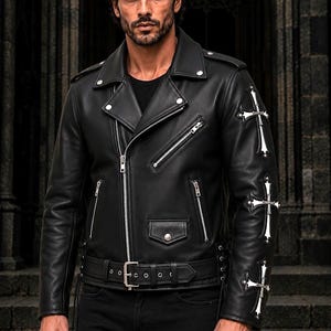 May include: A black leather motorcycle jacket featuring a wide notched collar, silver-tone metal zippers, and a buckled waist belt. The left sleeve is decorated with three white and silver cross-shaped emblems arranged vertically along the outer arm.