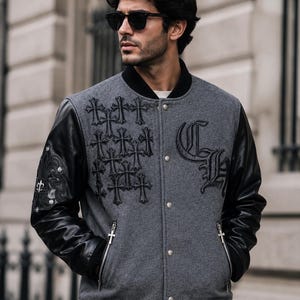 May include: A grey wool-blend varsity jacket with black leather sleeves, featuring black cross embroidery on the chest, a large gothic CH logo, silver-toned metal snap buttons, zippered pockets with cross-shaped pulls, and a black ribbed collar.
