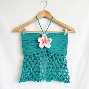 May include: A teal crochet halter top featuring a solid horizontal stitch pattern on the upper section and an open, net-like stitch pattern on the lower section. A white and pink crocheted flower is attached to the center of the neckline.