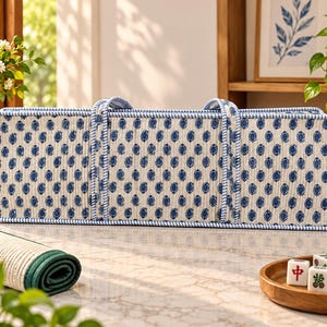 May include: A rectangular, quilted fabric storage bag featuring a cream-colored base with a repeating pattern of small, dark blue paisley-like motifs. The bag has two matching fabric handles and is trimmed with blue and white striped piping.