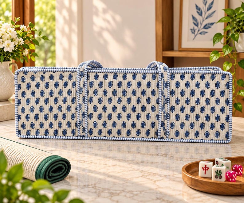 May include: A rectangular, quilted fabric storage bag featuring a cream-colored base with a repeating pattern of small, dark blue paisley-like motifs. The bag has two matching fabric handles and is trimmed with blue and white striped piping.