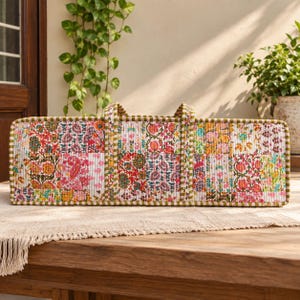May include: A rectangular quilted tote bag featuring a vibrant patchwork design with various floral and paisley patterns in shades of pink, orange, green, and white. The bag has two vertical fabric handles and a green and white striped trim.