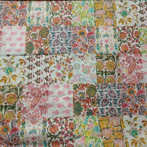 May include: A patchwork quilt featuring a grid of square fabric panels with diverse floral and paisley block-print patterns in shades of pink, orange, green, yellow, and blue on a white background, creating a multi-colored textile design.