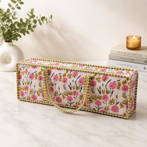 May include: A rectangular quilted fabric storage bin featuring a repeating floral pattern of pink flowers and green foliage on a light background. The bin has a structured shape with green and white striped fabric trim and two matching fabric handles.