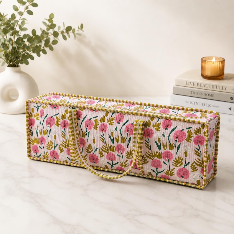 May include: A rectangular quilted fabric storage bin featuring a repeating floral pattern of pink flowers and green foliage on a light background. The bin has a structured shape with green and white striped fabric trim and two matching fabric handles.