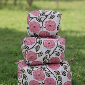 Peut inclure: Une pile de trois boîtes de rangement rectangulaires en tissu, dotées d'une base blanche avec un motif répétitif de fleurs roses et de feuilles vert foncé. Chaque boîte présente de petites languettes en tissu aux coins et une texture matelassée.