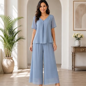 May include: A dusty blue two-piece set consisting of a short-sleeved blouse with a V-neckline and matching wide-leg trousers. The outfit is crafted from a lightweight, flowing fabric that drapes loosely, creating a relaxed silhouette.