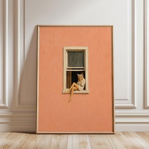 Op de afbeelding: Een ingelijste muurkunstprint met een effen perzikkleurige muur met één rechthoekig raam. Een figuur zit op de vensterbank, draagt een lichtgekleurd overhemd en leest een open boek, met de benen naar buiten gericht vanuit het kozijn.