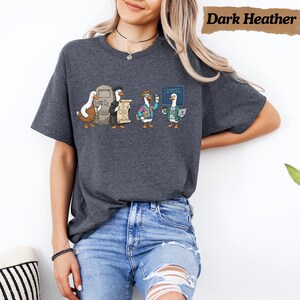 May include: A dark heather gray t-shirt featuring a graphic of four cartoon ducks dressed as different tech professionals. The ducks are depicted with a computer monitor, a scroll, a laptop, and a coffee mug. The text Dark Heather is visible.