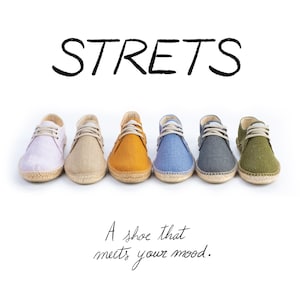 Può includere: Sei scarpe stringate con suole in iuta intrecciata disposte in fila, nei colori viola chiaro, beige, giallo senape, blu, grigio scuro e verde oliva. Il testo STRETS e A shoe that meets your mood. è stampato in nero sopra e sotto.