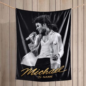 May include: A black and white rectangular blanket featuring a portrait of a performer singing into a microphone while wearing an unbuttoned white shirt and dark trousers. The gold script text Michael To NAME is printed at the bottom of the blanket.