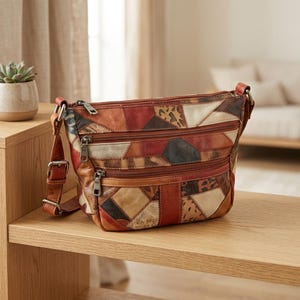 Puede incluir: Un bolso bandolera de cuero multicolor con un diseño de parches en varios tonos marrones, rojos y crema. El bolso incluye dos bolsillos delanteros con cremallera, un cierre superior de cremallera y una correa ajustable con herrajes metálicos.