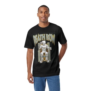 Peut inclure: Un t-shirt noir à manches courtes avec une impression graphique sur la poitrine. Le motif affiche le texte DEATH ROW dans une police métallique au-dessus d'une illustration d'une silhouette en costume argenté assise sur un trône doré.