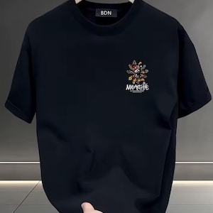 Peut inclure: Un t-shirt noir à manches courtes avec un col rond. La poitrine présente un petit motif coloré représentant un ours stylisé entouré de formes florales et abstraites, avec le texte "MKGARCHIVE" imprimé en blanc sous le motif.