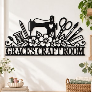 May include: A black metal wall sign featuring a sewing machine, scissors, pencil, ruler, and floral motifs. The text "GRACE'S CRAFT ROOM" is displayed in bold capital letters at the bottom of the decorative cutout design.