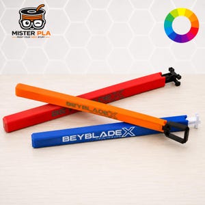 Può includere: Tre lanciatori a corda Beyblade X in rosso, arancione e blu. Ogni lungo strumento rettangolare in plastica presenta il logo Beyblade X stampato in bianco o grigio scuro. I lanciatori arancione e blu hanno impugnature alle estremità.
