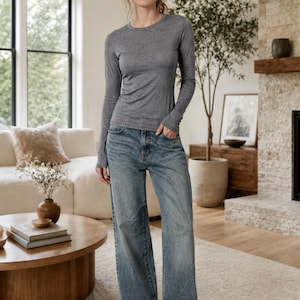 May include: A long-sleeve heather gray crew neck shirt paired with loose-fitting blue denim jeans and white sneakers. The shirt features a fitted silhouette with long sleeves, while the jeans have a wide-leg cut and a classic medium wash finish.