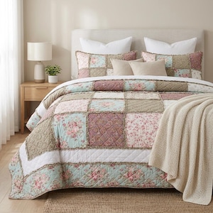May include: A patchwork quilt featuring a mix of floral and quilted fabric squares in shades of dusty rose, sage green, and cream. The quilt has frayed edges between the squares and is draped over a bed with two matching shams and white pillows.