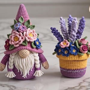 Puede incluir: Un gnomo de ganchillo con un sombrero morado adornado con flores rosas, azules y moradas, con barba y trenzas blancas, junto a una planta en maceta de ganchillo con lavanda morada y flores coloridas en una maceta amarilla y morada.