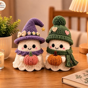 May include: Two crocheted ghost figures. The left ghost wears a purple witch hat with a small gold star, a bow, and tiny flowers, holding a pink pumpkin. The right ghost wears a green beanie with a pom-pom and heart patches, holding an orange pumpkin.