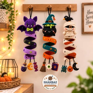 Può includere: Tre decorazioni di Halloween all'uncinetto da appendere, raffiguranti un pipistrello viola, un calderone nero con un cappello da strega color ottanio e una mummia color crema con un uccellino nero. Ogni figura ha una coda a spirale con piccoli ciondoli.