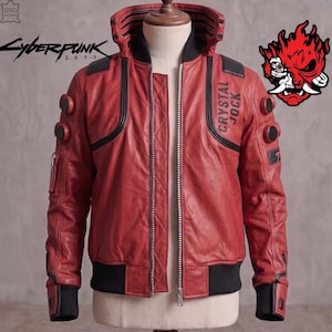 Op de afbeelding: Een rode leren jas met een hoge kraag, zwarte geribbelde boorden en zoom, en een ritssluiting aan de voorzijde. Op de borst staat de tekst CRYSTAL JOCK, terwijl de mouwen cirkelvormige accenten hebben. Een Cyberpunk 2077-logo en een rode oni-maskerafbeelding zijn zichtbaar.