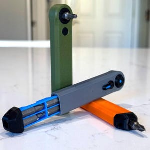 May include: Three handheld screwdriver tools with integrated bit storage. One is olive green, one is gray with a blue internal tray, and one is orange. Each tool features a black end cap and a metal screwdriver bit at the tip for manual use.