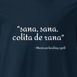 May include: A dark navy blue short-sleeved t-shirt featuring white text printed on the chest that reads "sana, sana, colita de rana" followed by the smaller text "- Mexican healing spell" in a clean, white serif font.