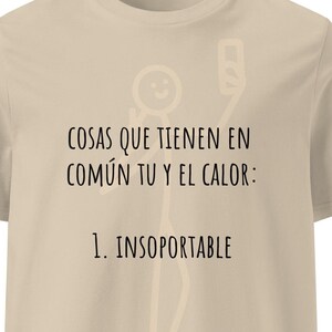 Könnte beinhalten: Ein beiges kurzärmeliges T-Shirt mit einer blassen Strichmännchen-Grafik und schwarzem Text, der lautet: COSAS QUE TIENEN EN COMÚN TU Y EL CALOR: 1. INSOPORTABLE. Das Design ist mittig auf der Brust des Kleidungsstücks mit Rundhalsausschnitt platziert.