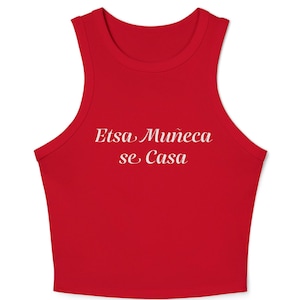 May include: A bright red sleeveless crop top with a high neckline and thick shoulder straps. The centre of the chest features the white text Etsa Muñeca se Casa written in a cursive script font. The garment has a simple, fitted silhouette.