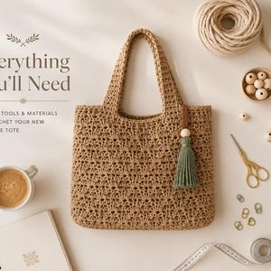 Peut inclure: Un sac fourre-tout en crochet beige avec un pompon vert sauge, entouré d'une pelote de fil, de perles en bois, de ciseaux dorés, de marqueurs de mailles, d'une aiguille, d'un mètre ruban, d'un carnet et d'un café, avec le texte Everything You'll Need.