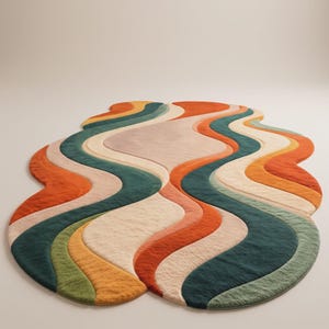 Op de afbeelding: Een vloerkleed met een onregelmatige, organische vorm voorzien van een reeks vloeiende, golvende banen in tinten diepblauwgroen, bosgroen, mosterdgeel, gebrand oranje en cr&egrave;me. Het oppervlak heeft overal een pluche, getextureerde pool.