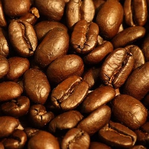 May include: Close-up of a pile of roasted coffee beans. The beans are dark brown and have a shiny, oily surface.