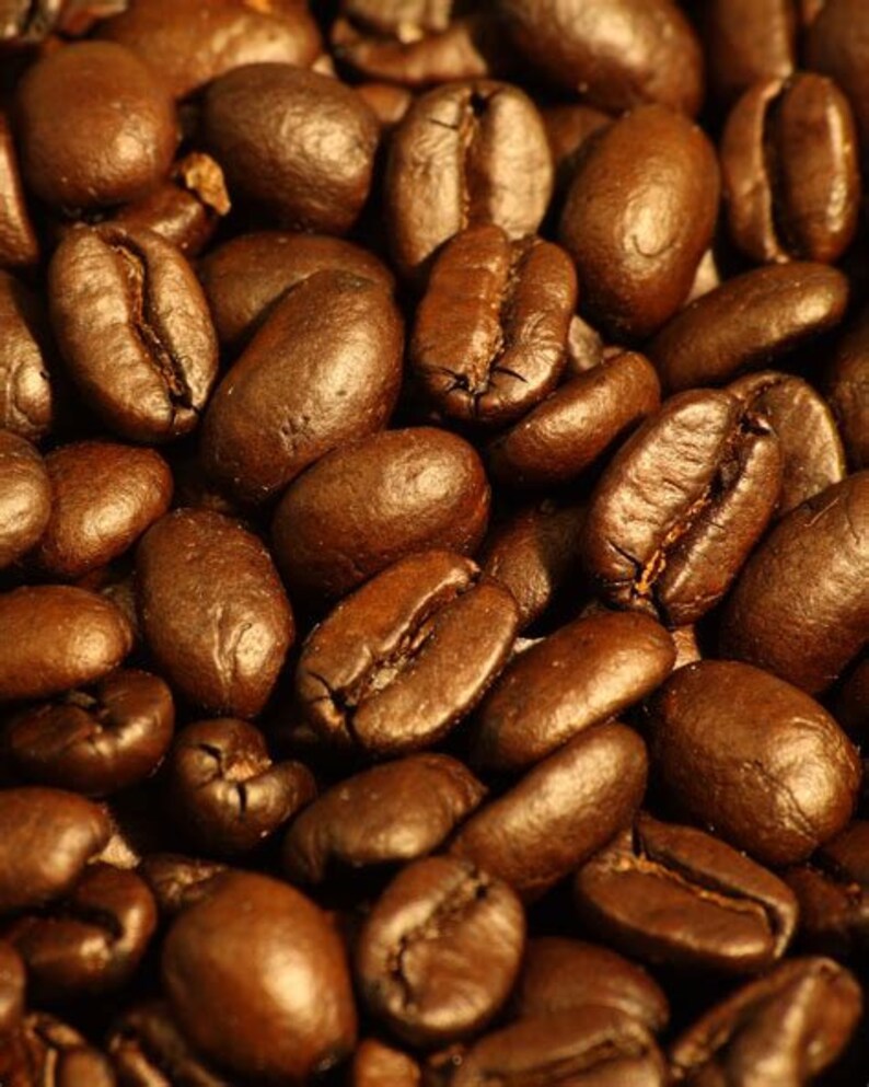 May include: Close-up of a pile of roasted coffee beans. The beans are dark brown and have a shiny, oily surface.