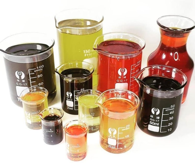 May include: Assortment of glass measuring cups filled with different colored liquids. The liquids are clear, yellow, orange, red, and black. The cups are marked with measurements in milliliters.