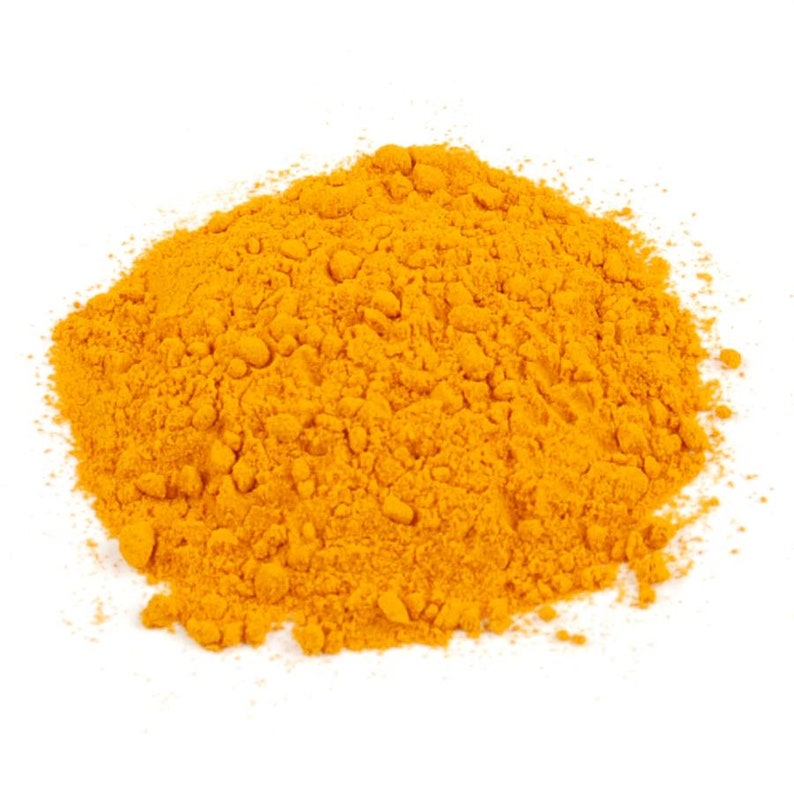 Puede incluir: Un mont&oacute;n de polvo de c&uacute;rcuma finamente molido con un color naranja dorado vibrante y saturado. La textura parece seca y granulada, formando una pila irregular y suelta con peque&ntilde;os grumos dispersos por la superficie de la especia.