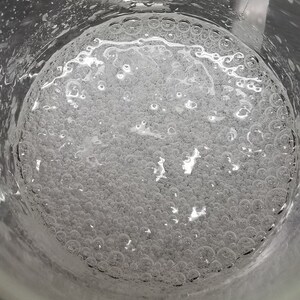 Puede incluir: Primer plano de un vaso de precipitados de vidrio transparente lleno de un l&iacute;quido transparente con muchas burbujas peque&ntilde;as.