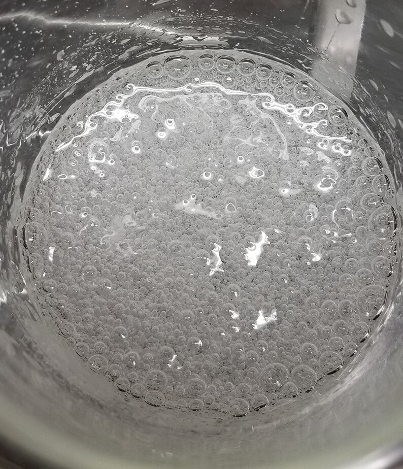 Puede incluir: Primer plano de un vaso de precipitados de vidrio transparente lleno de un l&iacute;quido transparente con muchas burbujas peque&ntilde;as.