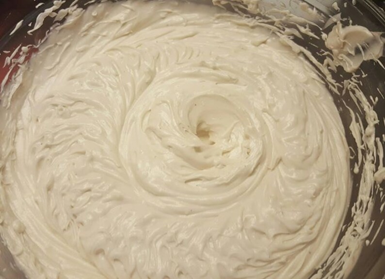 May include: A close-up of a white whipped cream frosting in a glass bowl. The frosting is smooth and creamy, with a swirl pattern.