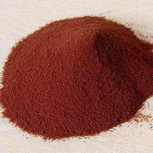 Puede incluir: Un mont&oacute;n de polvo finamente molido de color marr&oacute;n rojizo intenso con una textura granular. La sustancia est&aacute; apilada en un mont&iacute;culo redondeado, mostrando un color tierra oscuro y consistente en todo el volumen del material seco y suelto.