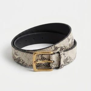 May include: A coiled belt featuring a snakeskin pattern in shades of beige, grey, and black. The belt includes a rectangular brass-toned metal buckle and a matching leather loop, with a solid black interior lining visible along the inner edge.